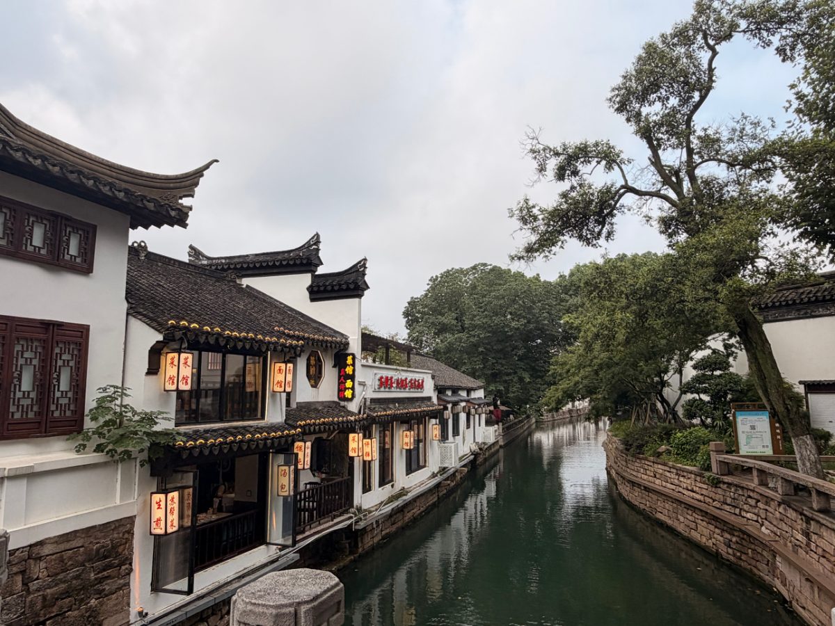 A quiet canal lined with white buildings, curved tile roofs and glowing lantern signs